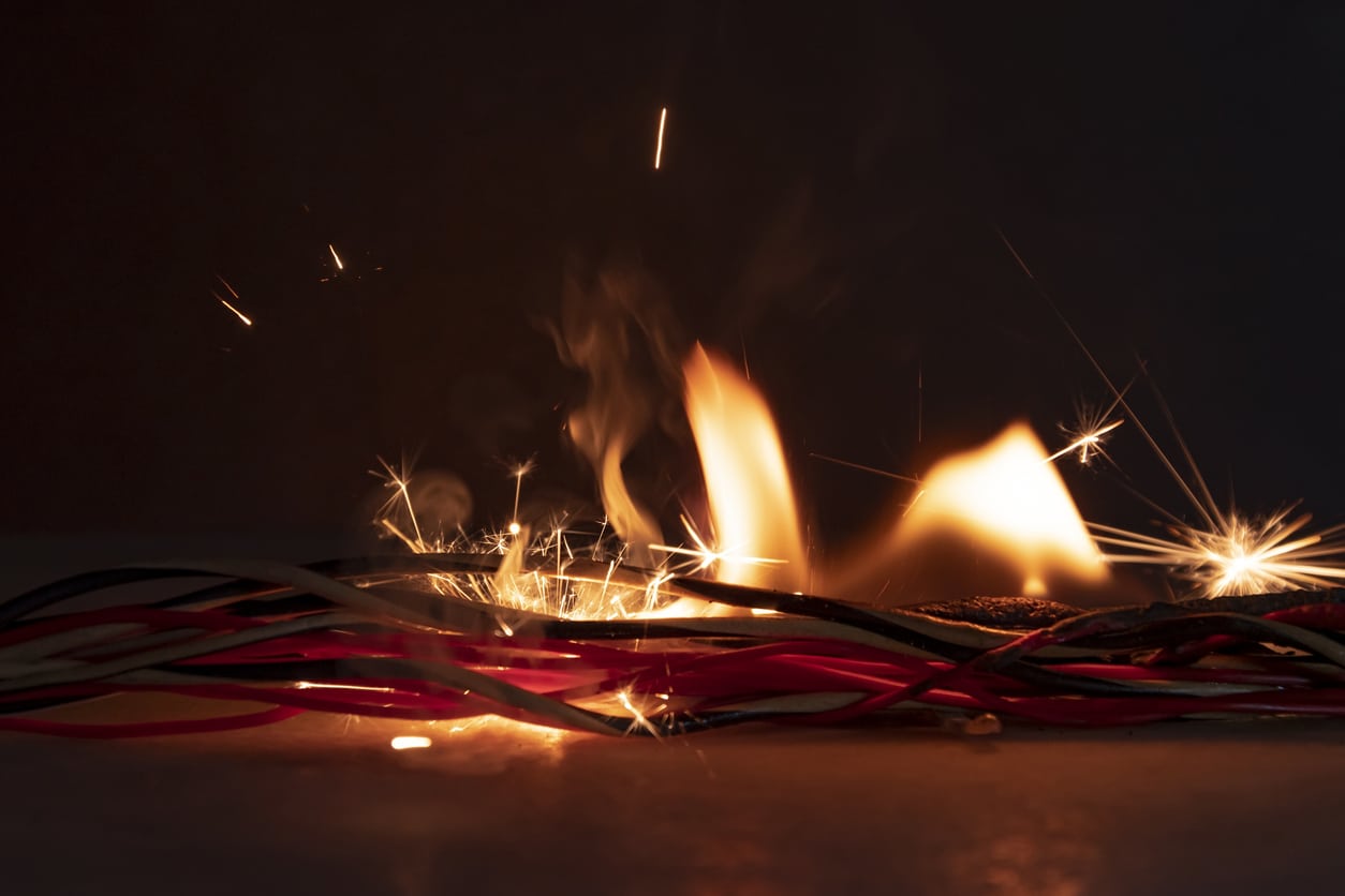 Image of the bottom of a Christmas tree, with a sparking electrical outlet in the background.