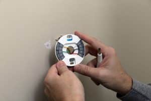 A licensed electrician installs a smart thermostat in a residential home. 